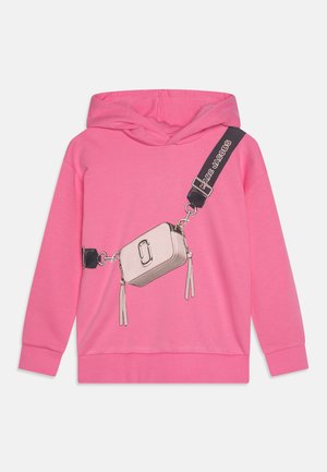 Haut à capuche rose vif présentant un graphique d'un sac bandoulière argenté avec une bandoulière noire et des pompons, fabriqué dans un tissu doux et extensible.