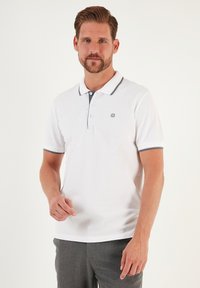 B�ílá polo košile s jednobarevným designem, kreativním modrým límcem a akcenty na rukávech, třemi knoflíky a malým logem na hrudi.