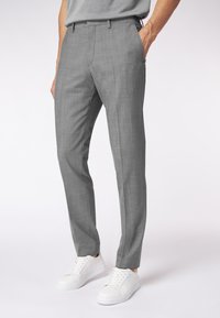 Graue maßgeschneiderte Hose mit strukturiertem Finish, seitlichen Taschen und schlanker Passform, kombiniert mit weißen Sneakers.