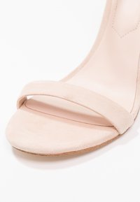 Sandale à talon en suède beige, dotée d'une large bride sur l'avant du pied et d'une semelle lisse et arrondie, avec un intérieur doux et des détails de couture minimalistes.