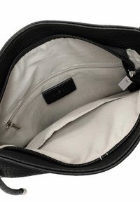 Black leather bag interior with a soft beige lining, featuring a zippered pocket and a fabric tag. The bag has a textured outer surface.