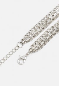 Svetlo siva kovinska veriga, ki vsebuje več povezanih niti in sponko za lobster. Gladka tekstura s stalnim sijajem in enotna zasnova.