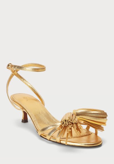 Sandale en satin doré avec un petit talon, dotée d'un accent de franges au niveau des orteils et d'une bride réglable à la cheville pour un ajustement sécurisé.