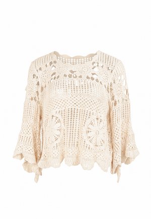 Blouse beige en crochet avec des motifs floraux et géométriques en ajouré, manches trois-quarts évasées et ourlet festonné.
