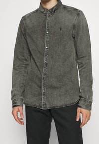 Långärmad skjorta i tvättad svart denim, med knäppning framtill, spetsig krage och diskret logotyp på bröstet. Slät textur.