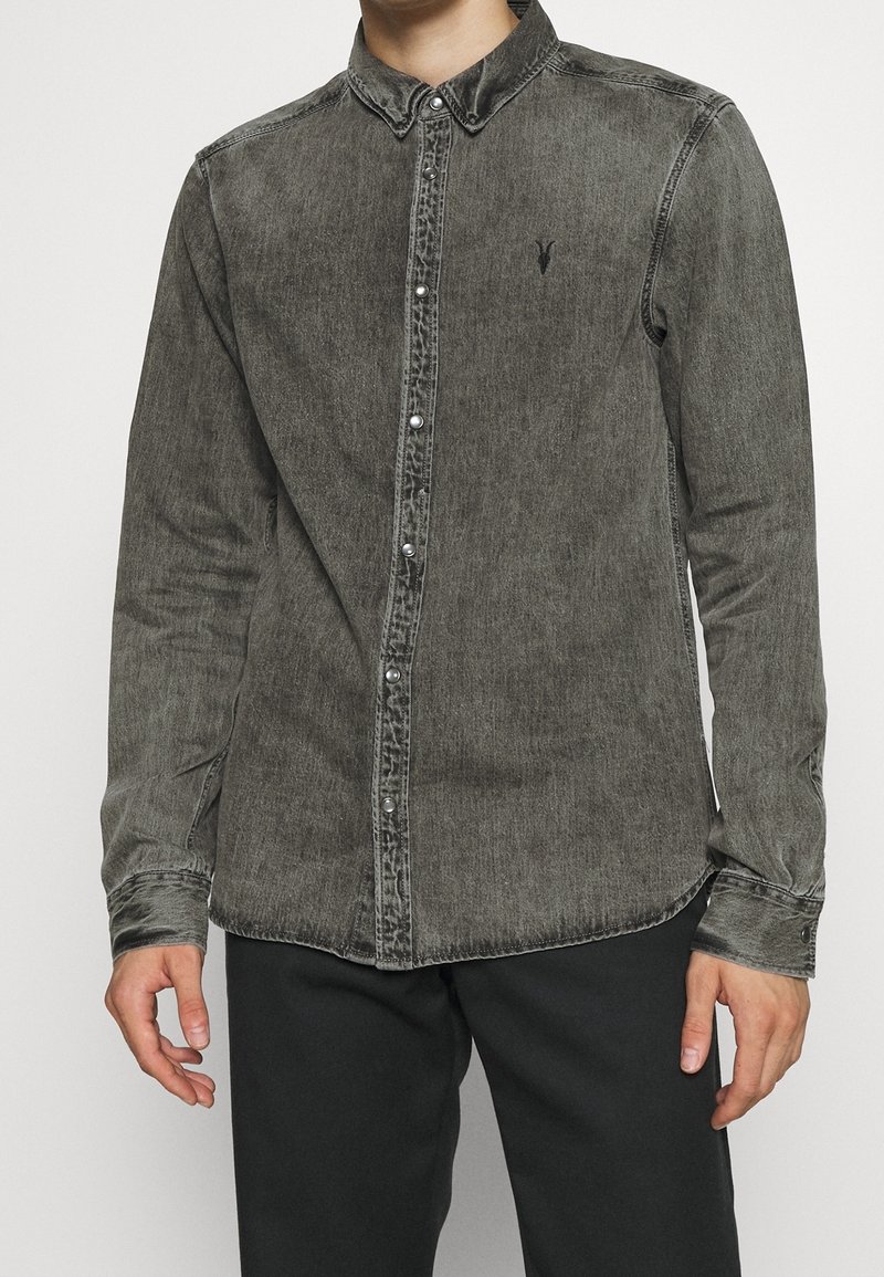 Långärmad skjorta i tvättad svart denim, med knäppning framtill, spetsig krage och diskret logotyp på bröstet. Slät textur.