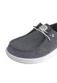 Scarpa slip-on grigia glitterata con suola bianca, caratterizzata da una punta arrotondata, tomaia in tessuto e dettaglio in pizzo nella parte frontale. Logo del brand visibile sul lato.
