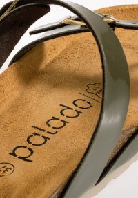 Grön glansig sandal med en mockainsåle, med en platt sula och en enkel remdesign. Fotbädden har präglad varumärkestext.