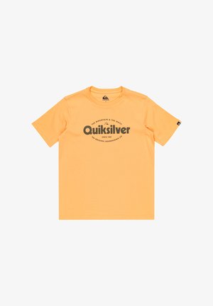 Pomarańczowa bawełniana koszulka z logiem "Quiksilver", zestawiona z oliwkowozielonymi szortami, czarno-białymi trampkami i czarnymi skarpetkami.