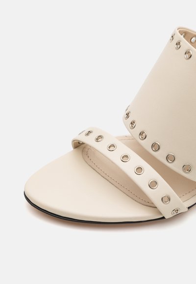 Beige leren sandaal met twee brede banden met metalen ogen, open teenontwerp en een platte zwarte zool. Gekenmerkt door een gladde textuur.