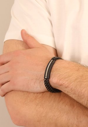 Schwarzes Kettenarmband mit einem strukturierten Band und einem glatten Silberakzent. Es verfügt über ein geflochtenes Design, das das Handgelenk ergänzt.