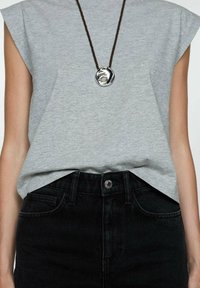T-shirt gris à manches courtes associé à un jean noir taille haute. Le t-shirt présente une coupe décontractée et un collier avec un pendentif texturé et rond.