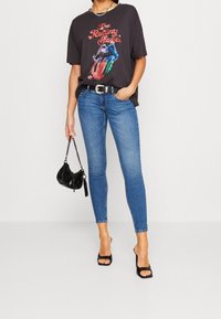 Camiseta gráfica negra con diseño de los Rolling Stones, jeans skinny azules, cinturón negro, bolso negro y tacones abiertos negros.