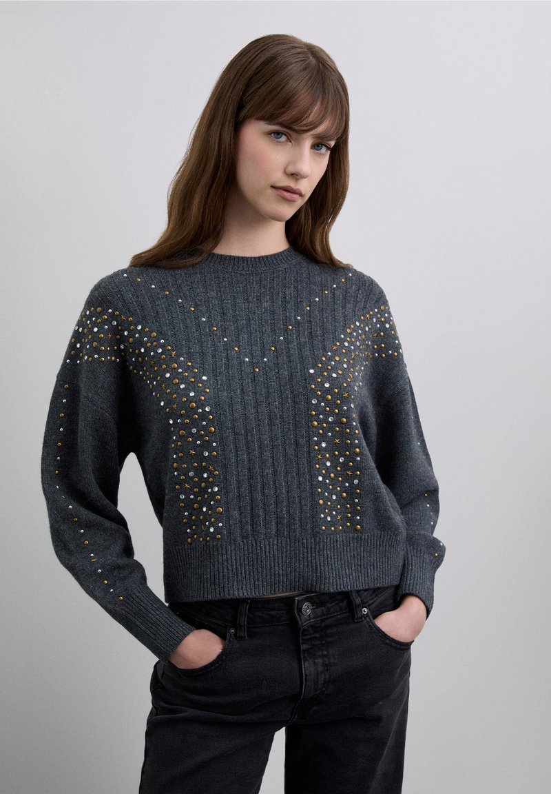 Maglione grigio lavorato a maglia con trama a coste, caratterizzato da ornamenti metallici in oro, argento e bianco, e un collo girocollo comodo.