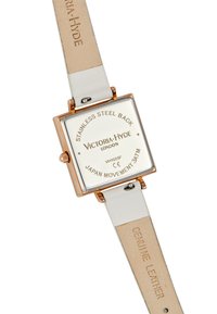 Reloj cuadrado con correa de cuero genuino blanca, acentos en rosa dorado y fondo de acero inoxidable. Presenta una esfera blanca con el grabado de la marca.