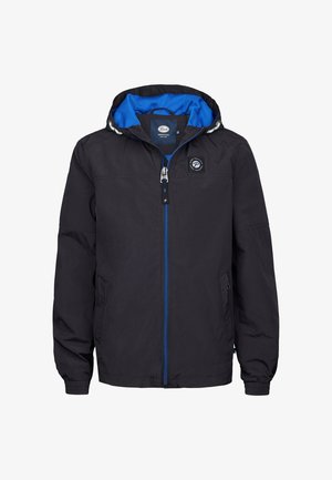 Chaqueta ligera negra con capucha azul, cremallera frontal y detalle de logo. Llevada con jeans azules y zapatillas blancas, de pie frente a un fondo neutro.