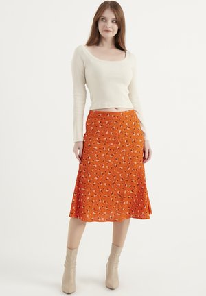 Orange floral midi skirt with pleats, featuring a fitted waist and lightweight fabric. Paired with a ribbed cream long-sleeve top and beige boots.