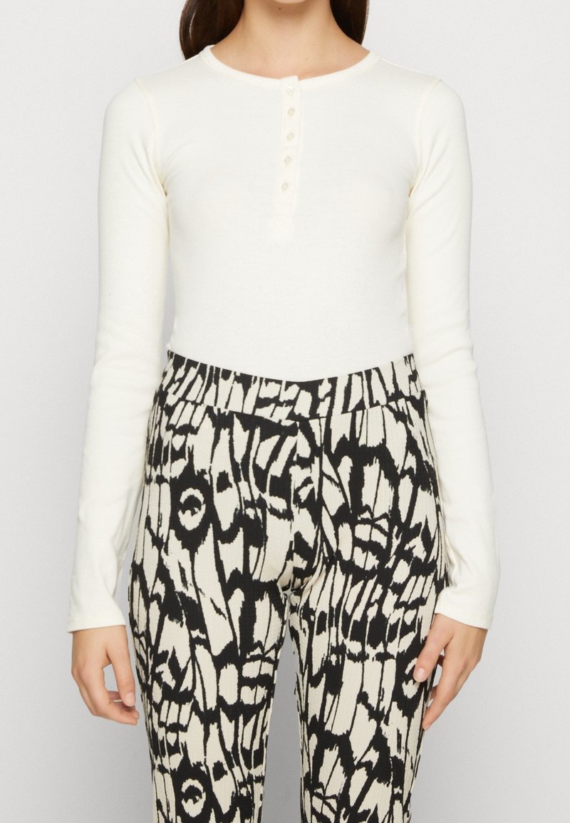 Vit långärmad topp med knäppning, kombinerad med svarta och krämfärgade mönstrade ribbade byxor med abstrakta mönster.