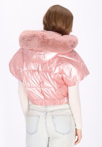 Różowa pikowana kurtka z połyskującym wykończeniem i kołnierzem z sztucznego futra. Krótki fason z krótkimi rękawami i marszczonym dołem. Widoczne jasnoniebieskie dżinsy.