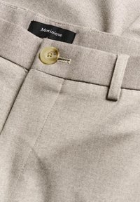 Pantaloni bej dintr-un material texturat cu un finisaj neted, având închidere cu buton, bucle pentru curea și un eticheta de marcă vizibilă.