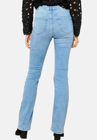 Vaqueros acampanados de mezclilla azul claro con una cintura alta, dos bolsillos traseros y un desvanecimiento sutil en toda la tela, combinados con una blusa negra texturizada.
