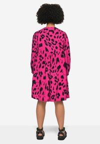 Roze panterprint jurk met lange mouwen, verzamelde taille en een uitlopende silhoutte. Heeft een geweven stof en zwarte accenten.