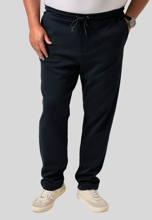 Marineblaue Sweatpants mit elastischem Bund und Kordelzug. Verfügt über Seitentaschen und ein geschnittenes Bein-Design. Getragen mit hellen Sneakers.
