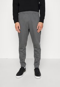 Grå sweatshirtbyxor med en slim fit, elastisk midja och avsmalnande ben. Har sidostråk med en svartvit design. Kombineras med svarta sneakers.