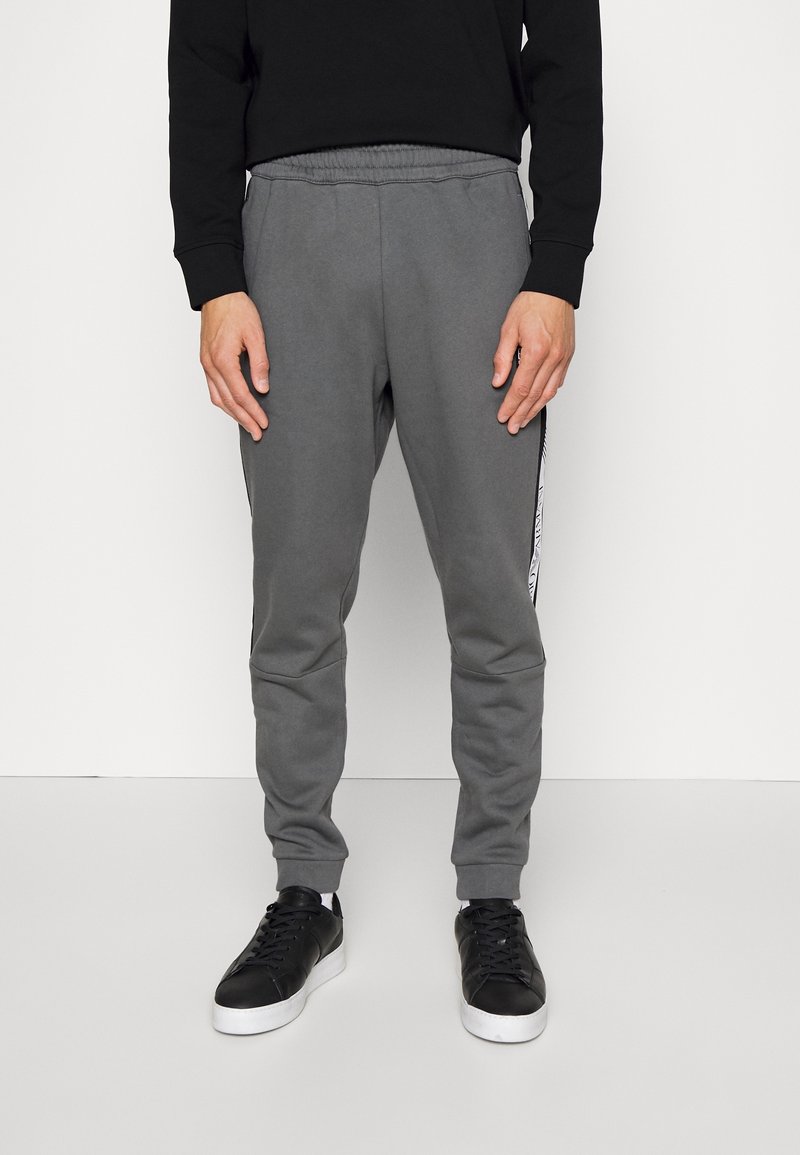 Grå sweatshirtbyxor med en slim fit, elastisk midja och avsmalnande ben. Har sidostråk med en svartvit design. Kombineras med svarta sneakers.