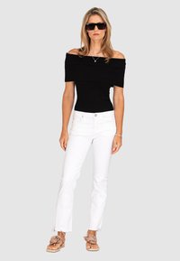 Black off-the-shoulder top with ribbed texture, paired with white flared jeans and beige sandals featuring a flower accent.