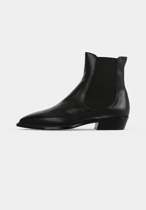 Bottine Chelsea en cuir noir avec panneau latéral élastique et petit talon bloc sur un fond clair uni.