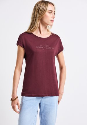 Mörkröd bomullströja med rullade korta ärmar, med vit text "Bekväma Sommarkvällar" på framsidan. Mjuk textur, avslappnad passform.