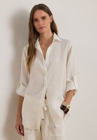 White linen shirt with a collared neck, button front, roll-up sleeves, and a loose fit. Notable is the soft texture and lightweight appearance.