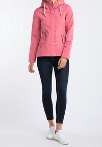 Roze waterdichte jas met capuchon, zilveren drukknoopsluitingen, twee zijzakken en verstelbare koordjes, gecombineerd met donkere skinny jeans en witte sneakers.