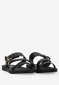 Sandali neri piatti con più cinturini, dettaglio della fibbia in tono oro e una soletta a superficie liscia. Design semplice con stile minimalista.