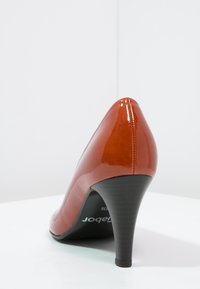 Escarpin à talon haut en cuir verni orange brûlé brillant. Design épuré avec un bout pointu et un talon noir effilé. Semelle intérieure plate.