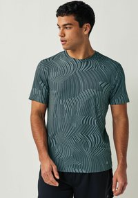 Grøn atletisk t-shirt lavet af struktureret materiale, med et bølger-mønster i mørkere nuancer, korte ærmer og rund halsudskæring.