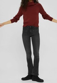 Pull en maille rouge avec un col haut et des manches texturées, associé à un jean noir taille haute avec deux poches arrière et une coupe slim.
