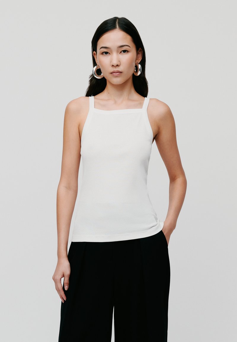 Top de bumbac alb, ajustat, cu bretele subțiri, decolteu pătrat și țesătură texturată. Poartă-l cu pantaloni negri largi. Design simplu, fără modele.