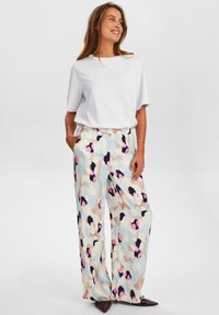 Pantaloni a gamba larga multicolore con un tessuto morbido e testurizzato, caratterizzati da motivi astratti in blu, rosa e beige, abbinati a un semplice top bianco.
