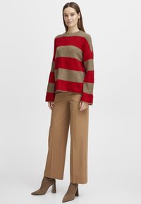 Maglione a righe rosse e beige, lavorato a maglia, con maniche lunghe, abbinato a pantaloni beige a gamba larga e stivaletti con tacco abbinati.
