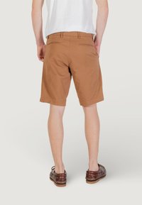 Shorts marron en tissu à texture lisse, au design classique, avec deux poches arrière et une coupe droite, portés avec des chaussures marron.