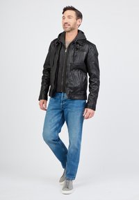 Zwarte leren jas met een grijze hoodie eronder, gecombineerd met lichtblauwe jeans en grijze sneakers. Casual outfit met gelaagde texturen.