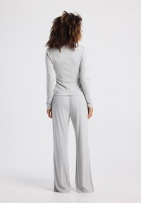 Graues Longsleeve-Oberteil und passende weite Hose, aus weichem Stoff gefertigt, mit körpernahem Schnitt und Naht im Rücken für zusätzliche Struktur.