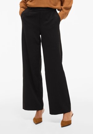 Czarne spodnie o szerokich nogawkach z gładkiego materiału, z wysokim stanem i bocznymi kieszeniami. Do tego beżowe mule z ostro zakończonym noskiem.