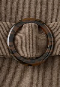 La tela marrón acanalada presenta un gran anillo circular de carey colocado sobre una sección doblada del material.