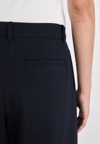 Pantaloni blu navy con taglio dritto, dotati di una tasca posteriore e una texture liscia. La cintura è rifinita per un look aderente.