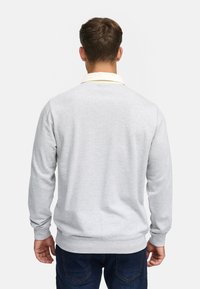 Lys grå sweatshirt med rund hals, lange ærmer, ribbede mansjetter og kant. Har en kontrasterende gul krave. Glat tekstur.