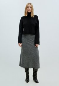 Zwart cropped sweater met geribbeld textuur, gecombineerd met een grijze maxi rok. Model draagt zwarte kniehoogte puntige laarzen. Eenvoudig en monochroom kleurenschema.