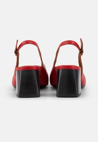 Red leather block-heeled sandals with ankle strap. Smooth texture with a contrasting brown leather accent at the base and a solid black heel.